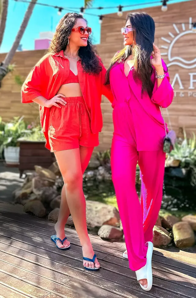 Duas amigas de vermelho e de rosa caminhando juntas num deck, em pose com amiga