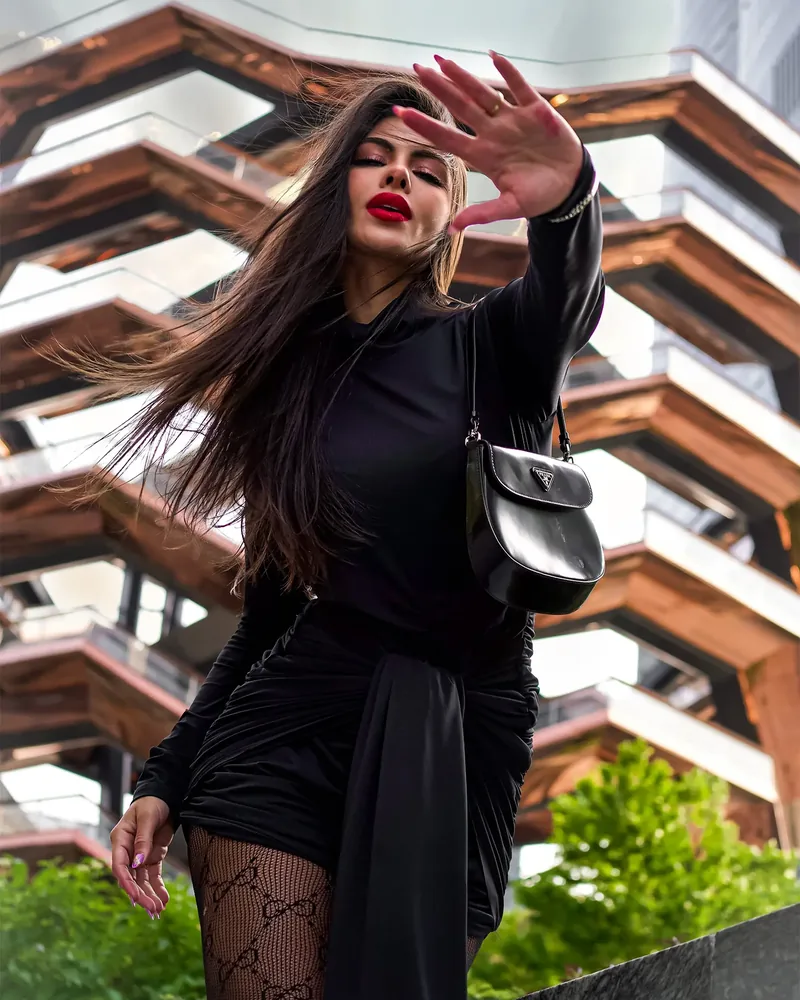 Depois do preset: Catarina de preto, com o cabelo ao vento, em frente a uma escultura de escadas
