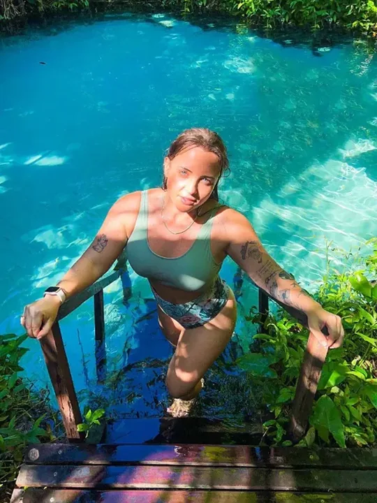 Mulher subindo a escada de madeira de um rio de água azul-turquesa