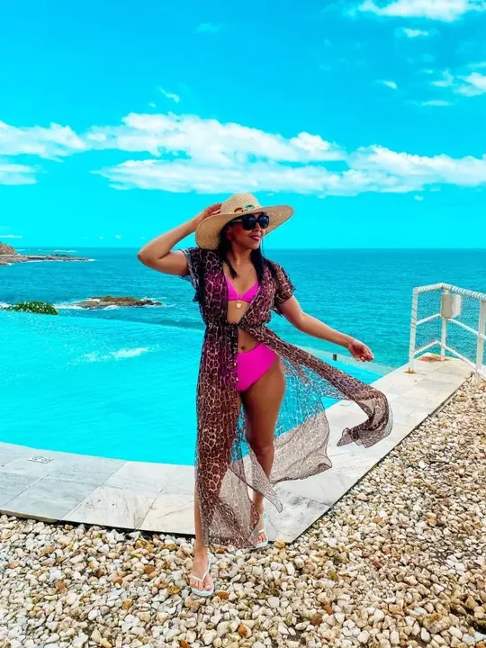 Mulher de chapéu e saída de praia num deck de frente para o mar