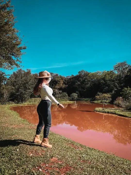 Mulher de chapéu caminhando à beira de um lago avermelhado