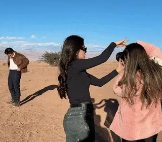 Catarina Leal no deserto ajeitando a pose de uma amiga enquanto outra pessoa fotografa